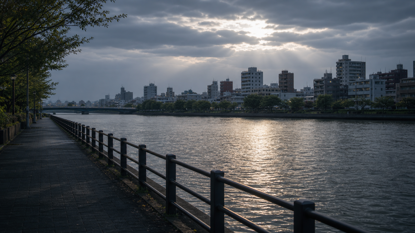 架空の休日の川沿い。曇り空の切れ間から光が差し、空いた遊歩道と川面が静かに広がっている。